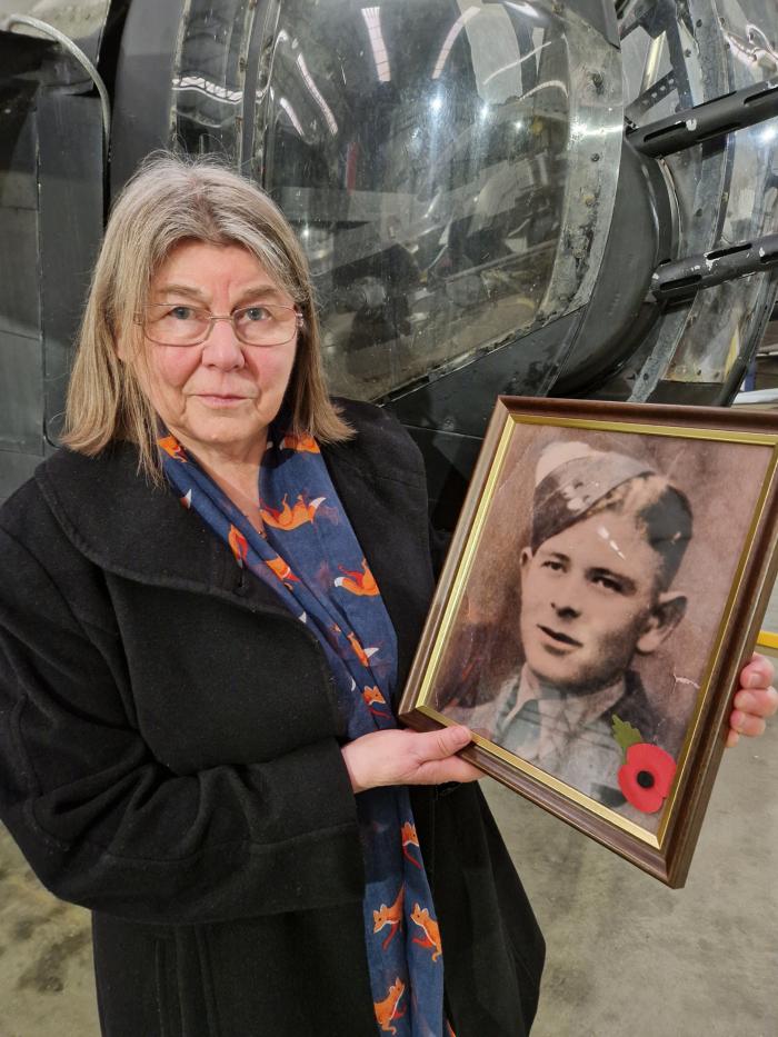 Celia standing by the rear gun turret of YAM’s Halifax Mk.III, holding a photo of her uncle