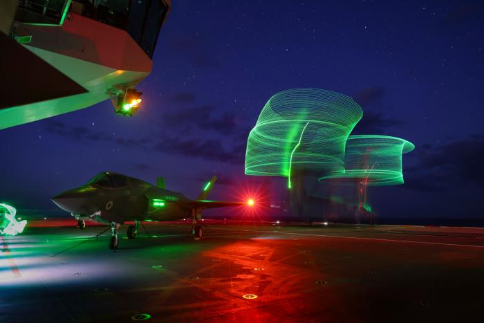 A long exposure image of a US Air Force CV-22B Osprey, based at RAF Mildenhall, conducting deck landing training on HMS Queen Elizabeth. In the foreground is a 617 Sqn F-35B Lightning.